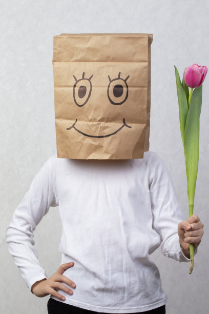 孩子站着，头上顶着一个纸板箱，面带微笑，手里拿着一朵郁金香。图片下载