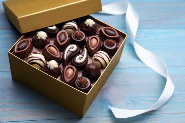 在浅蓝色的木桌上打开一盒美味的巧克力糖果和彩色丝带图片下载
