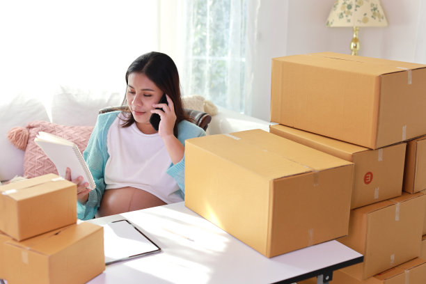 迷人快乐的亚洲孕妇坐在那里使用移动智能手机，用平板电脑为客户检查订单。准妈妈在怀孕期间为婴儿的出生做准备和工作。图片下载