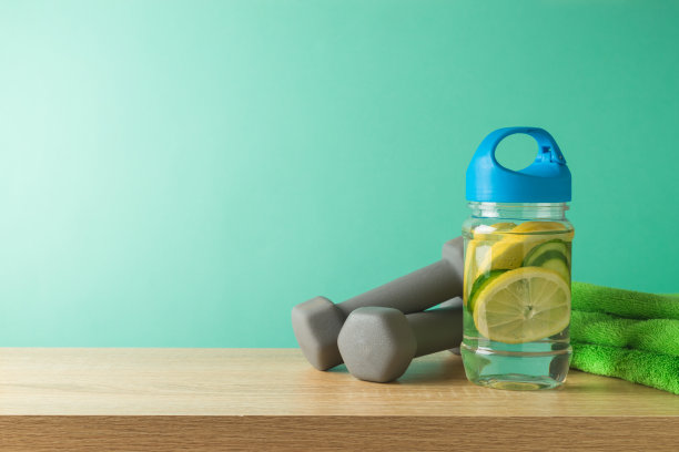健身背景与注入柠檬和黄瓜水，毛巾和哑铃在木桌上图片下载
