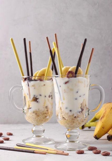两杯加巧克力和香蕉的格兰诺拉麦片，在灰色的背景上用小棍装饰图片下载