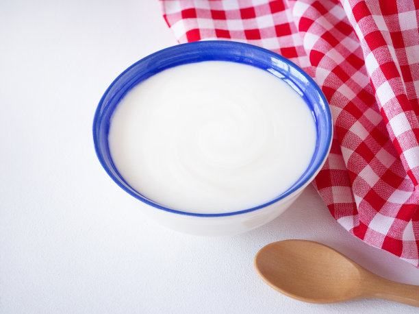 自制的希腊酸奶或酸奶油在蓝色的碗和木勺和红色方格织物或餐巾在白色的木制背景。图片下载