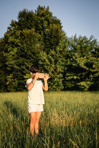 站在绿色田野里的女孩用手机拍照图片下载
