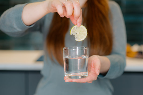 一个女人把一片柠檬扔进一杯水中的特写镜头图片下载