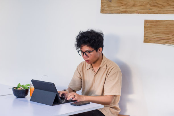 一头卷发的亚洲年轻人坐在咖啡馆里使用数码产品图片下载