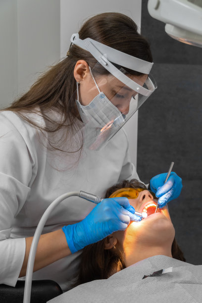 女牙医在诊所为年轻女病人治疗牙齿。牙医使用牙钻及打磨牙齿时须戴上口罩。现代牙科诊所的牙科程序。细长立式照片图片下载