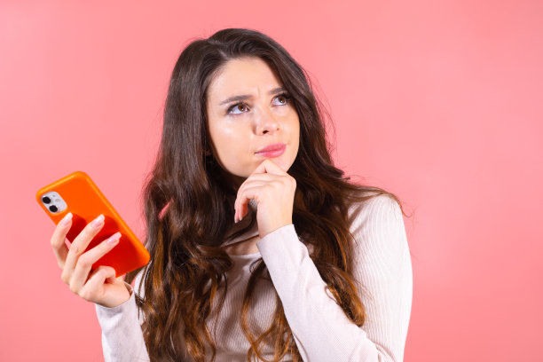美丽体贴的女人的肖像与智能手机在粉红色的背景图片下载