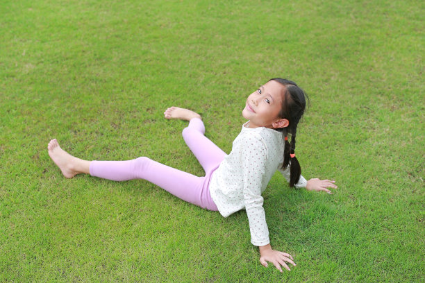 微笑的亚洲小女孩躺在花园的绿色草坪上。小孩躺在草地上看着相机。图片下载