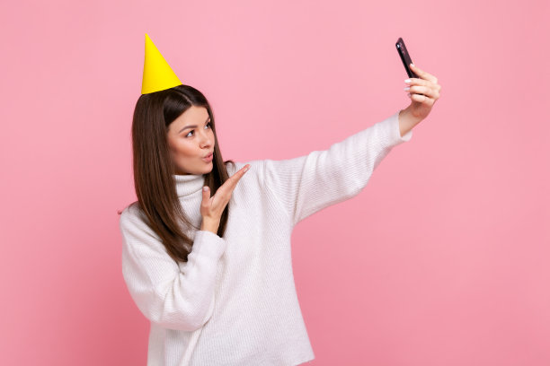 迷人的黑发女孩在派对上自拍或直播，发送飞吻。图片下载