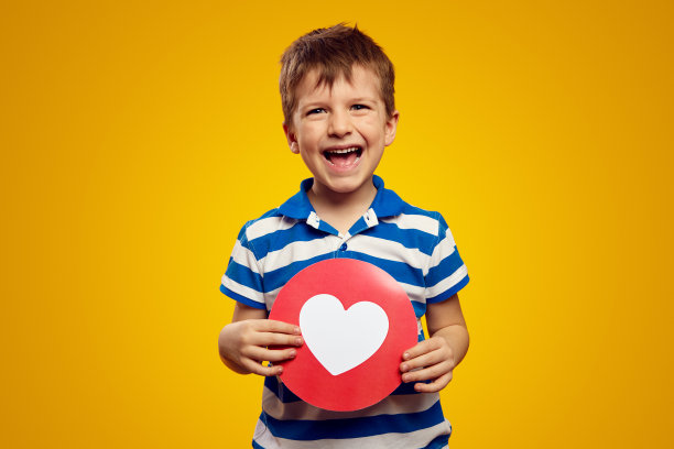 可爱的孩子穿着蓝色条纹polo衫，在黄色的衬托下显示出社交网络的心形图标图片下载