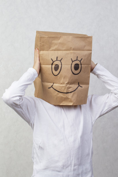 这个男孩的头上有一个纸板箱，上面画着一个有趣的笑脸。图片下载
