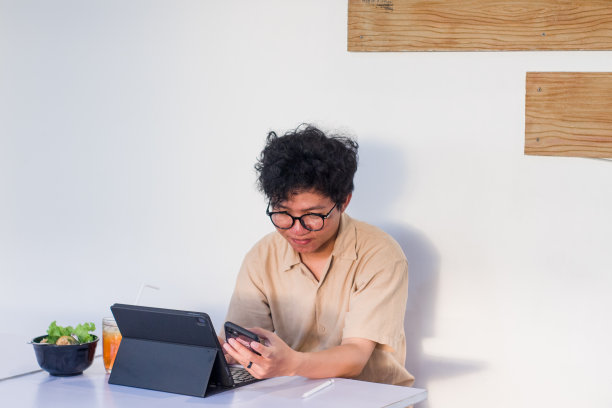 一头卷发的年轻亚洲男子坐在咖啡馆里使用电子设备工作图片下载