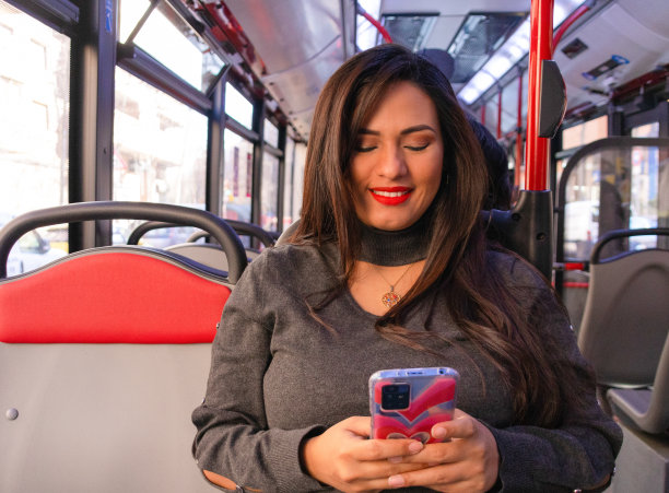 年轻的拉丁女子微笑着在她的手机上打字和乘公共汽车旅行图片下载