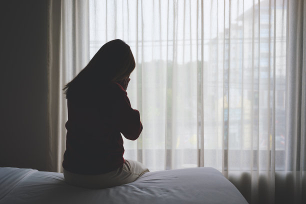 一个女人坐在卧室的床上哭泣的后视图图片下载