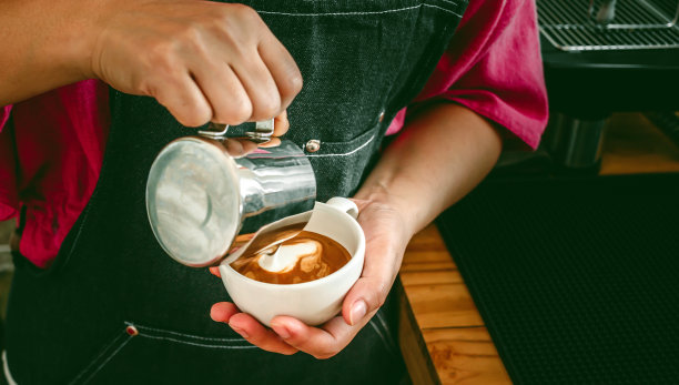 咖啡师在制作卡布奇诺时往咖啡里加牛奶。咖啡师制作卡布奇诺，专业调酒师准备咖啡饮品图片下载