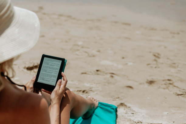 一名女子在沙滩上用电子阅读器看书图片下载