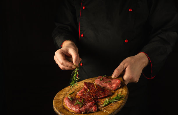 厨师在烤生牛排前加入迷迭香。准备午餐的烤肉。菜谱或菜单的黑暗空间图片下载