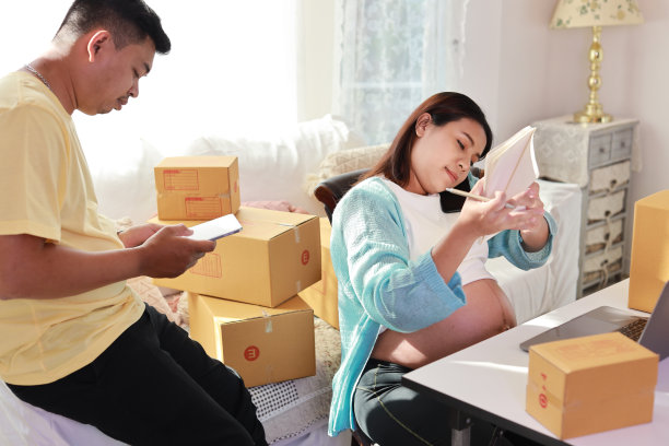 亚洲夫妇进行箱子包装工作，年轻孕妇坐着使用平板电脑和智能手机记录客户订单，丈夫一同工作图片下载