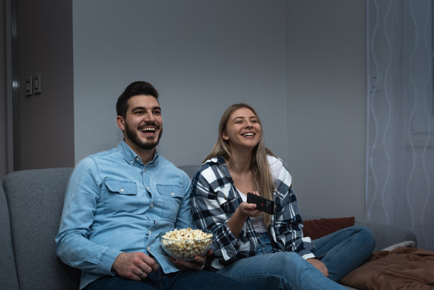 在家看电视。一对恩爱的夫妇躺在沙发上，一边吃爆米花，一边欣赏电影或电视电影图片下载