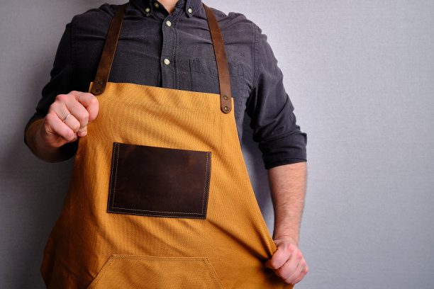 一个穿着厨房围裙的男人。厨师从事烹饪工作。穿着制服和防护服。食品服务方面的工作。专业烹饪。绿色面料围裙，休闲时尚服装。英俊的面包师摆姿势图片下载