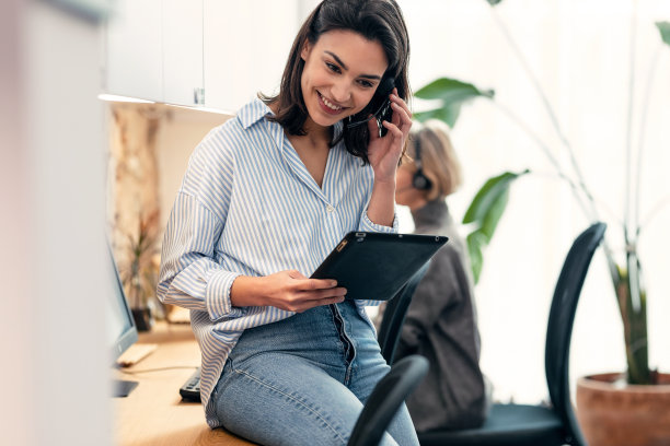 漂亮的女接线员在办公室里一边用无线耳机一边看数码平板电脑图片下载