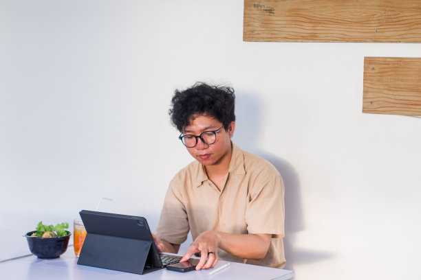 一头卷发的年轻亚洲男子坐在咖啡馆里使用电子设备工作图片下载