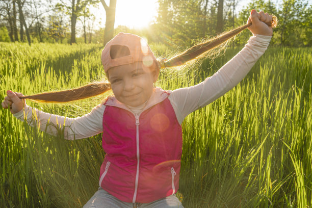 一个快乐的女孩坐在茂密的绿草地上图片下载