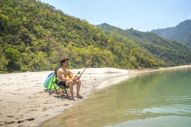 光膀子的游客坐在折叠椅上在湖里钓鱼图片下载