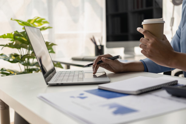 在办公室里，坐在木桌前用笔记本电脑工作的年轻女性是一名商人，她分析文件和图表，用笔记本电脑和计算器工作。远程图片图片下载