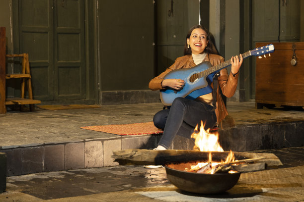 一个女人在室外的火堆旁弹吉他。图片下载