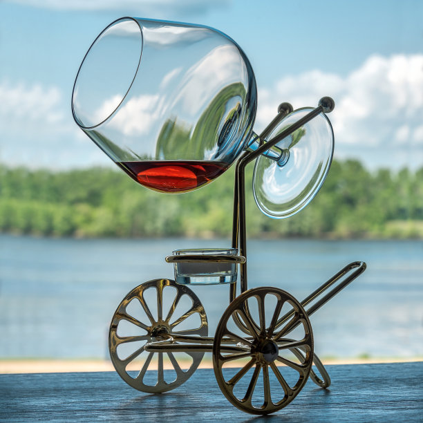 一杯白兰地，放在一个特殊的支架上，用蜡烛加热饮料，以森林和河流的自然景观为模糊的背景。图片下载