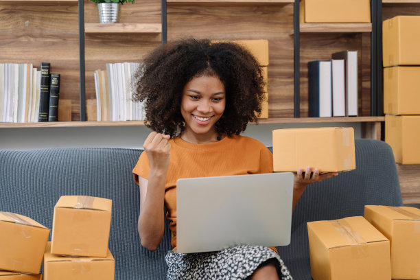 快乐的年轻女企业家，在家里用智能手机和笔记本电脑查看网上购物商店的订单后，对销售成功微笑，在线商业和电子商务的概念。图片下载