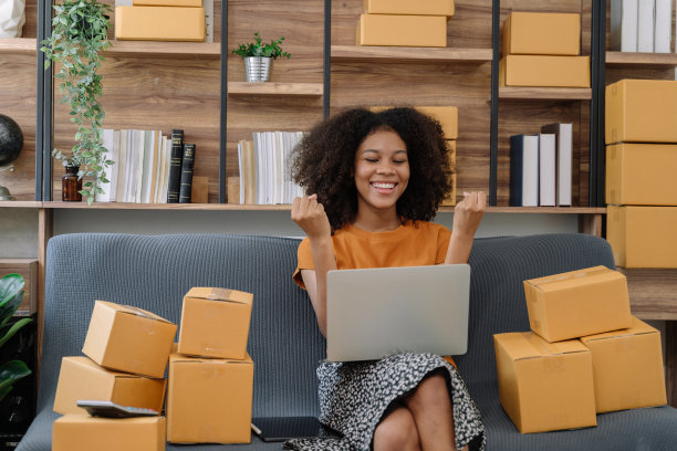 快乐的年轻女企业家，在家里用智能手机和笔记本电脑查看网上购物商店的订单后，对销售成功微笑，在线商业和电子商务的概念。图片下载