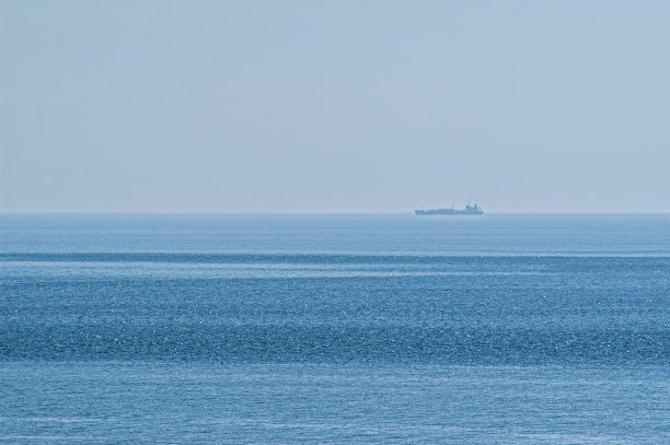 在一个阳光明媚的夏日，一艘货船从地平线上驶过。图片下载