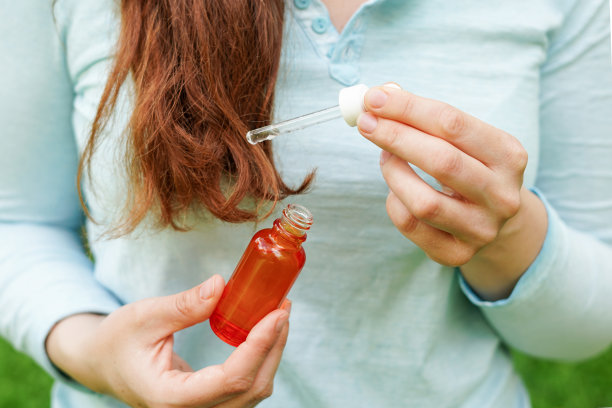 年轻女子用红色玻璃瓶装的天然有机精油涂在头发上。水疗和美容仪式。皮肤护理图片下载