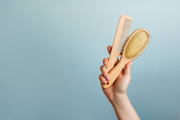 女子手持两把木制发刷，蓝色背景，头发护理，复制空间图片下载