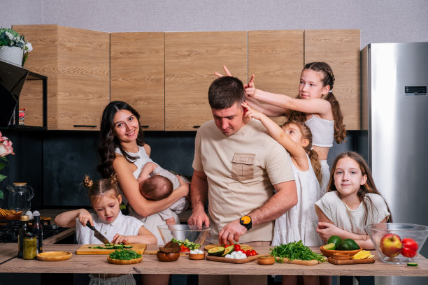 一个大家庭——妈妈、爸爸、4个女儿和一个儿子在一个现代化的厨房里一起准备午餐沙拉。大家庭在一起的概念。图片下载