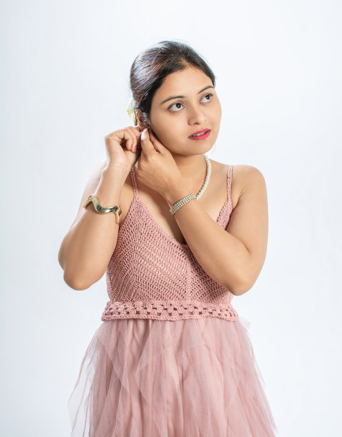 一个快乐的年轻女子的肖像在粉红色的合身和耀斑，意大利吊带网裙，戴着她的耳环图片下载