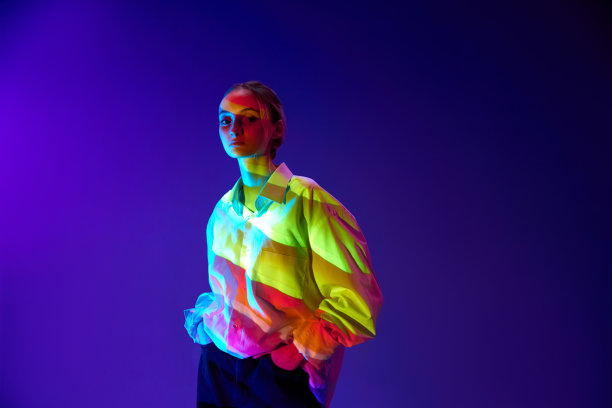 年轻时尚女孩的肖像，多色霓虹灯滤镜反射在身体上，摆姿势，看着紫色背景的相机图片下载