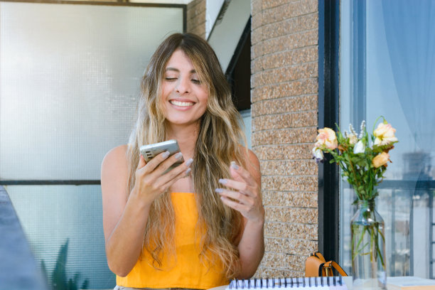 年轻的哥伦比亚女子站在公寓阳台上微笑着用手机。图片下载
