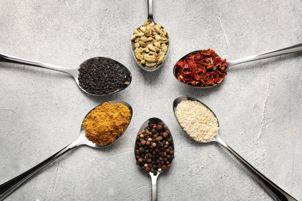 浅灰色的桌子上平放着盛着不同香料的金属勺子图片下载