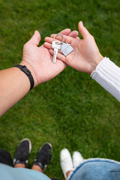 一个年轻家庭手中的新房子或公寓里的带钥匙链的金属房子形状的钥匙。买房带来的幸福。垂直的照片。图片下载
