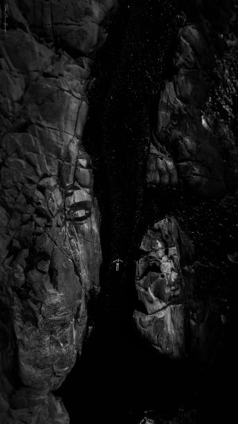 这张黑白照片是一条河周围的岩石和一个漂浮在水中的人图片下载