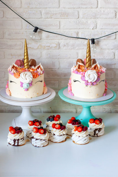 两个金角独角兽蛋糕，奶油漩涡，马卡龙和蛋白霜，一套迷你巴甫洛娃蛋糕，在白色的桌子上有新鲜的浆果图片下载
