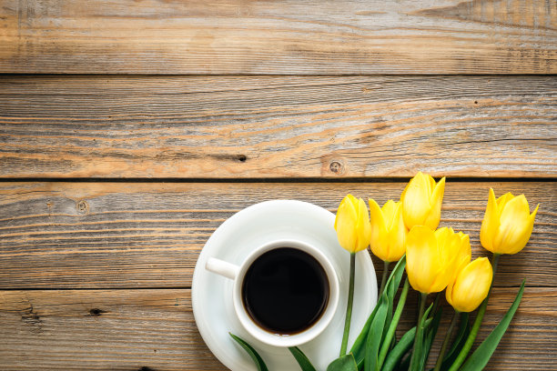木制背景上的黄色郁金香花束和一杯咖啡，俯视图。图片下载