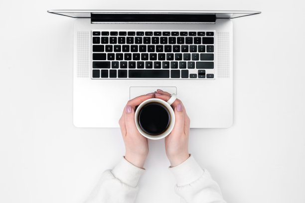 女性手中的一杯咖啡和一台白色背景的笔记本电脑，俯视图。图片下载