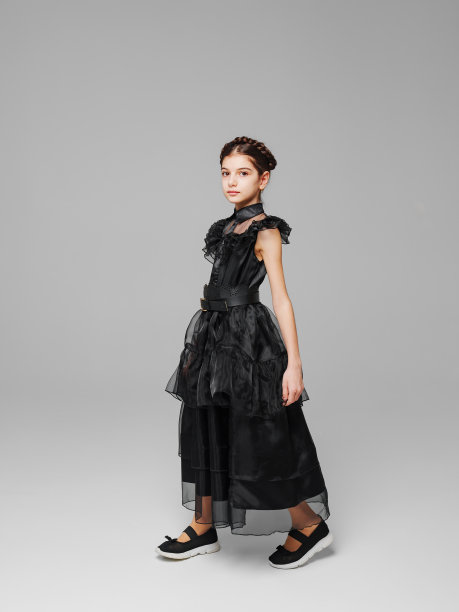 可爱的十几岁的女孩，在灰色的背景下，穿着一条黑色的曲线美长裙，扎着小辫子。图片下载