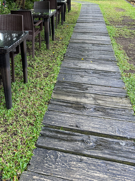 特写图片:回收的塑料柱、枕木、草坪上的花园小径、户外家具内衬的木纹效果板、一排带有藤编椅子的玻璃顶花园露台桌子，这些都是前景的重点图片下载