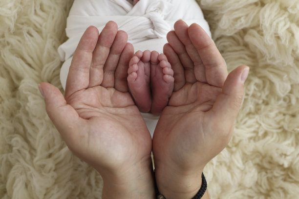 新生儿的脚放在父母的手掌上。父亲和母亲的手掌托着新生婴儿的脚，上面盖着一条白色的弗洛卡蒂毯子。孩子的脚趾、脚后跟和脚的照片。图片下载
