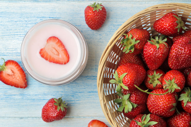美味的草莓酸奶装在罐子里，鲜熟的草莓放在浅蓝色的木桌上。俯视图图片下载